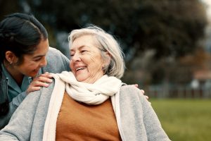 Caregiver helping woman with disability in park for support, trust and care in retirement. Nurse talking to happy senior patient in wheelchair for rehabilitation, therapy and conversation in garden.