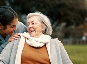 Caregiver helping woman with disability in park for support, trust and care in retirement. Nurse talking to happy senior patient in wheelchair for rehabilitation, therapy and conversation in garden.