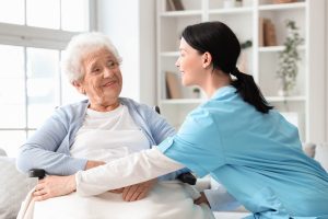 Female nurse caring about senior woman in wheelchair at home